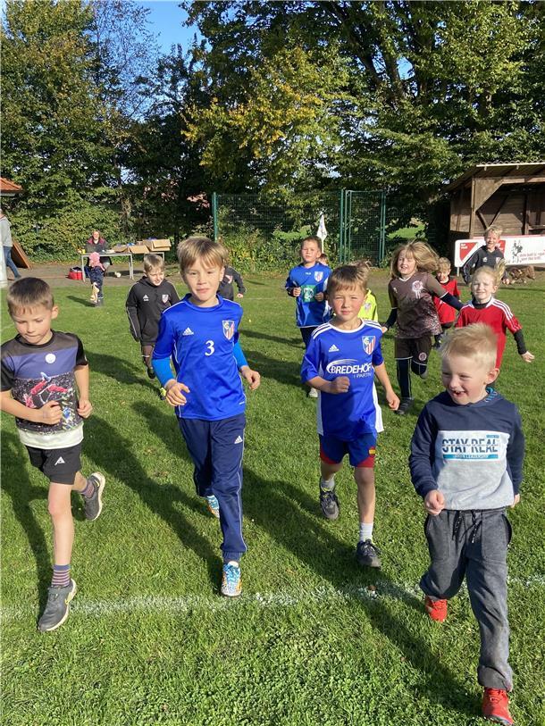 Kinder in Sport- und Trainingskleidung laufen auf einem Sportplatz.