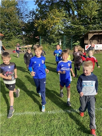 Kinder in Sport- und Trainingskleidung laufen auf einem Sportplatz.
