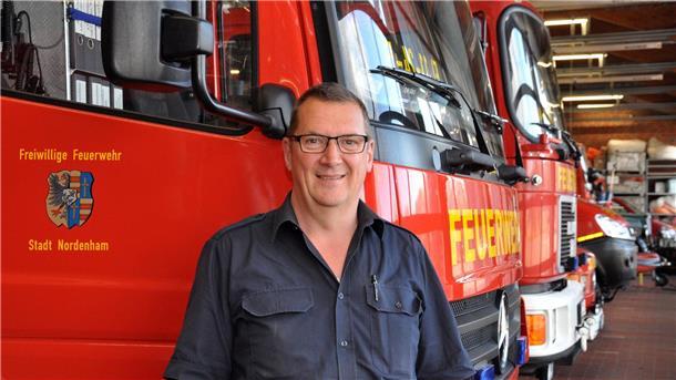 Ein Mann mit Brille steht vor mehreren Feuerwehrautos.