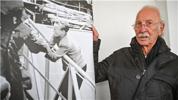 Ein älterer Mann steht neben einer großformatigen Schwarz-Weiß-Aufnahme. Die Aufnahme zeigt ihn als jungen Lehrling, wie er an einer Gangway Elvis Presley um ein Autogramm bittet.