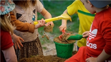 Vier Kinder füllen einen Eimer mit Sand.