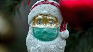 Weihnachtsschmuck in Form eines Weihnachtsmannes hängt mit Mund-Nasen-Schutz an einem Tannenbaum.   