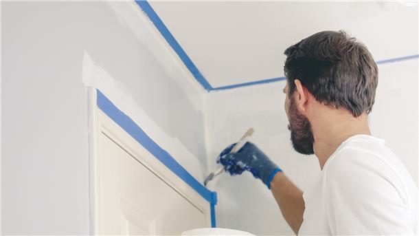 Zimmerwände streichen wie ein Profi – kein Problem! Ein Maler hat Türrahmen und Deckenleisten abgeklebt, um sauber streichen zu können.