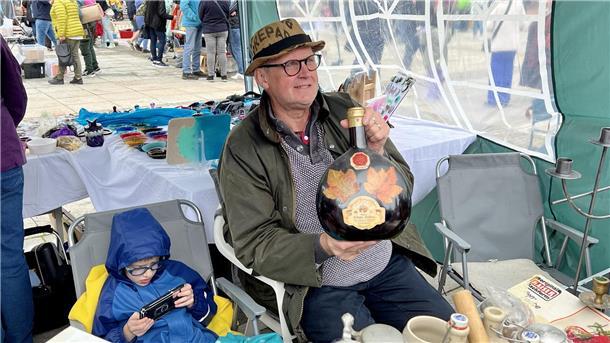 Regenschauer bremsen die Flohmarkt-Besucher aus, Verkäufer bleiben gut gelaunt Mann mit Weinflasche