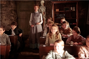 Eine lächelnde Lehrerin in einem Klassenzimmer mit mehreren Schülern. Alexandra Lamy (Mitte) als Louise Violet in einer Szene des Films „Louise und die Schule der Freiheit“.