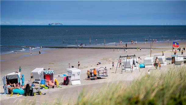 Touristen sitzen bei sonnigem Wetter in Strandkörben am Strand