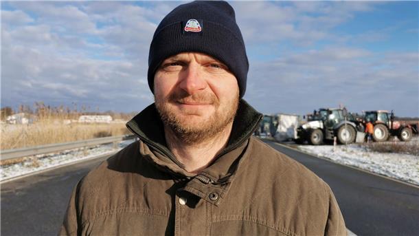 Mann mit Mütze und Winterjacke vor Traktoren im Hintergrund