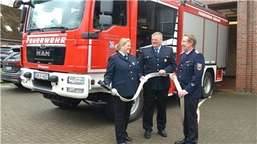 Eine Frau und zwei Männer stehen vor einem Feuerwehrauto.