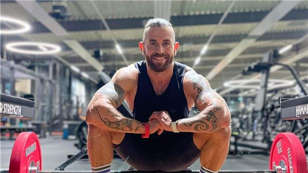 Mann kniet in einem Fitnessstudio vor einer Langhantel.
