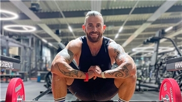 Mann kniet in einem Fitnessstudio vor einer Langhantel.