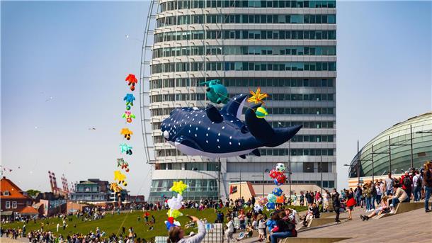 Bunte Drachenkunst am Weserdeich und in den Havenwelten Menschen beobachten bunte Riesendrachen am Himmel beim Drachenfestival in Bremerhaven vor dem markanten Sail City Gebäude und den Havenwelten.