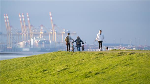 Eine Person mit Hund und zwei Radfahrer genießen die Aussicht am Lunedeich in Bremerhaven.