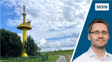Ein gelber Turm: Es ist ein Radarturm. Er steht auf einer grünen Wiese an grün blühenden Bäumen. Der Deich führt an ihm vorbei, ebenso ein Radweg.