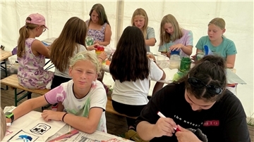 Kinder sitzen an Tischen und malen und basteln. 