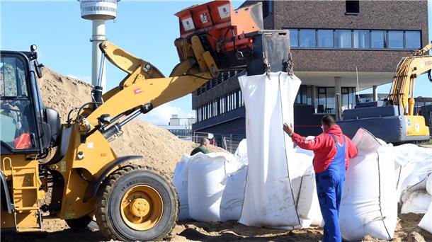 Arbeiter befüllen mit einem Radlader Sandsäcke. 