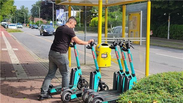 Ein Mann stellt E-Scooter an einer Bushaltestelle auf. 