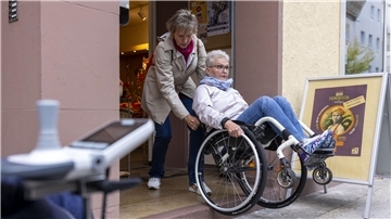 Eine Frau hilft einer Rollstuhlfahrerin beim Weg in ein Café.