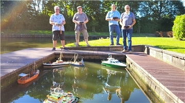 Vier Männer stehen an einem Wasserbecken und steuern ihre Schiffsmodelle.