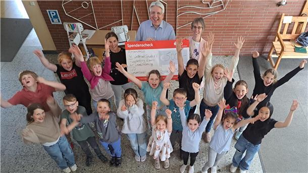 Das Foto zeigt viele Grundschüler und drei Erwachsene mit einem großen Scheck. Es ist bei einer Scheckübergabe in der Grundschule St. Willehad in Nordenham entstanden.