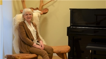 Eine Frau sitzt auf einer Holzbank neben einem Klavier.