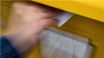 Eine Frau wirft einen Brief in einen Briefkasten.