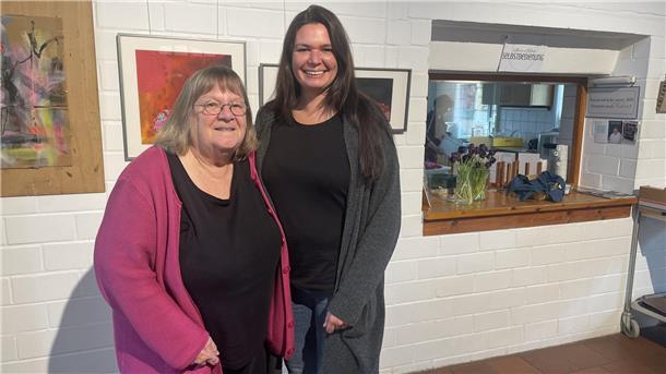 Zwei Damen stehen vor einer Wand mit Bildern. Anke Coldewey (links) führte rund 25 Jahre das Café in der Seefelder Mühle. Nun wird Wiebke Stromitzky ihre Rolle übernehmen.
