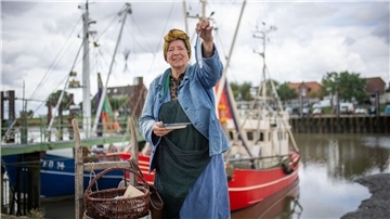 Annegret Martens preist als Fischhändlerin Minna im Fedderwardersieler Hafen Heringe an.