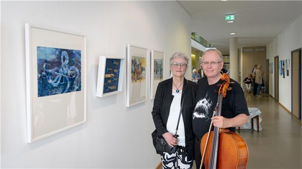 Annemarie Arndt und Josander Schück zeigen ihre Meeresbilder in Bremerhaven Kunstwerke an der Wand, Frau und Mann mit Instrument