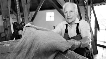 Ein älterer Mann hantiert auf einem Schwarz-Weiß-Foto in einer historischen Mühle mit einem Jutesack. Anton Günter Reumann aus Stollhamm ist im Alter von 87 Jahren verstorben.