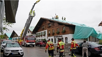 Arbeiter und Feuerwehrleute beseitigen die Unwetter-Schäden im oberbayerischen Bad Bayersoien. Bei dem Unwetter wurden viele Dächer beschädigt.