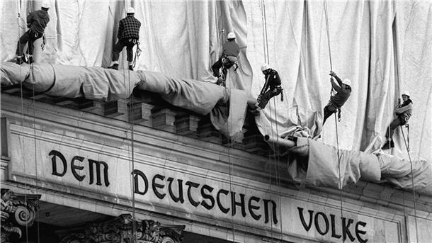 ARCHIV - 23.06.1995, Berlin: Gewerbekletterer rollen die Verhüllungsplanen für den Berliner Reichstag vom Giebel des Bauwerks ab. Direkt über dem Haupteingang und der Schrift "Dem Deutschen Volke" fällt bei der Aktion des Verpackungskünstlers Christo der Stoff entlang der Säulen zu Boden. (zu dpa "Vor 25 Jahren verhüllten Christo und Jeanne-Claude mit «Wrapped Reichstag» für zwei Wochen den späteren Bundestag") Foto: Wolfgang Kumm/dpa +++ dpa-Bildfunk +++