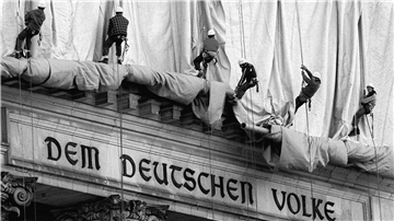 ARCHIV - 23.06.1995, Berlin: Gewerbekletterer rollen die Verhüllungsplanen für den Berliner Reichstag vom Giebel des Bauwerks ab. Direkt über dem Haupteingang und der Schrift "Dem Deutschen Volke" fällt bei der Aktion des Verpackungskünstlers Christo der Stoff entlang der Säulen zu Boden. (zu dpa "Vor 25 Jahren verhüllten Christo und Jeanne-Claude mit «Wrapped Reichstag» für zwei Wochen den späteren Bundestag") Foto: Wolfgang Kumm/dpa +++ dpa-Bildfunk +++