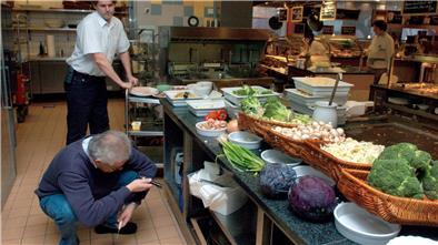 Hygienemängel im Restaurant: Wird Bremerhaven zu wenig kontrolliert? Ein Mann hockt mit einer Taschenlampe in einer Restaurantküche.