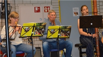 Drei Musikerinnen und Musiker sitzen nebeneinander und spielen Blockflöten in unterschiedlichen Größen. Vor ihnen stehen Notenständer mit gelben Mappen.