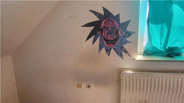Dreckige Wände und ein Heizkörper in einer Wohnung. An die Wand wurde der Kopf einer Videospielfigur gemalt.