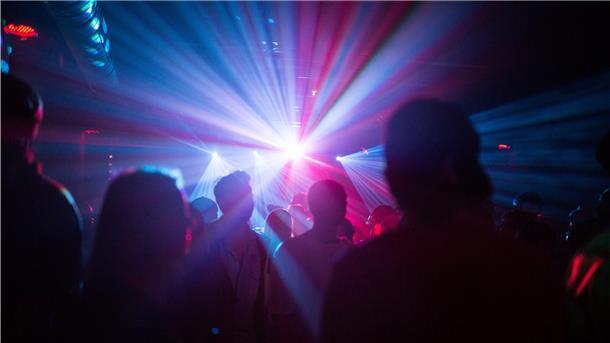 Tanzende Menschen in grellem Licht der Club-Atmosphäre.