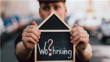 Ein Mann hält ein Schild mit einem Wohnungsgesuch in der Hand.