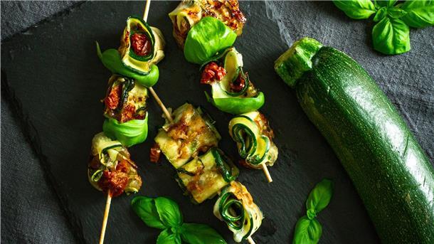 Grillen – viel mehr als nur Fleisch Auch lecker für die Grillparty: Zucchinischeiben werden mit Mozarella und getrockneten Tomaten belegt, dann aufgerollt und schließlich auf Holzspießchen fixiert.