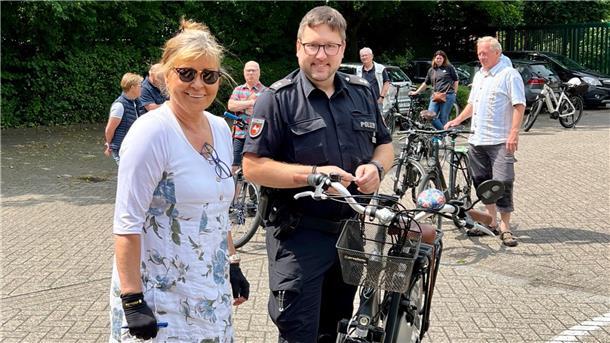 Ein Polizist codiert ein Fahrrad, die Besitzerin steht daneben.