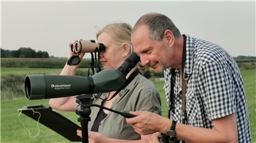 Ein Mann und eine Frau gucken durch ein Spektiv und ein Fernglas.