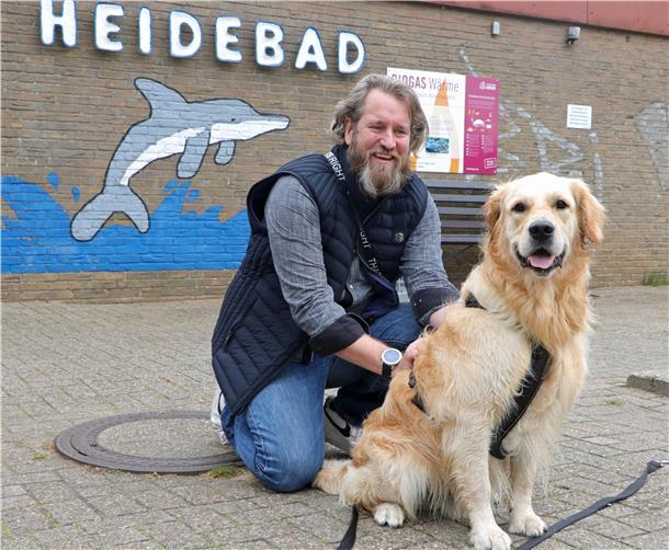 Ein Mann hockt mit seinem Hund auf dem Boden