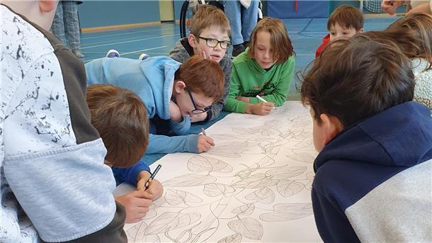 Kinder schreiben mit Stiften auf ein großes Plakat, auf dem eine Bohnenranke aufgemalt ist.