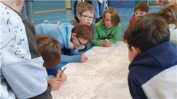 Kinder schreiben mit Stiften auf ein großes Plakat, auf dem eine Bohnenranke aufgemalt ist.