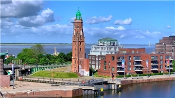 Blick auf einen Leuchtturm mit einer Fassade aus rotem Backstein und einer grünen Spitze.