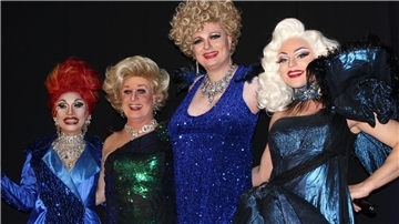 Vier Dragqueens stehen zusammen auf einer Bühne und lächeln.