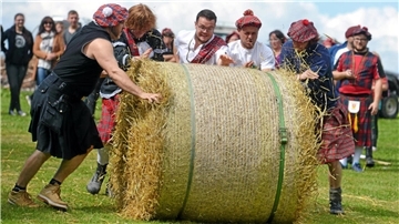Junge Männer rollen einen Heuballen. 