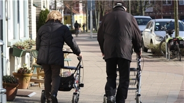 Zwei ältere Menschen schieben ihren Rollator über den Fußweg.