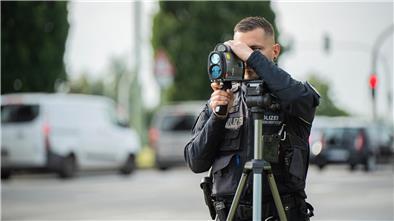 Speedweek: Wie es Temposündern in Bremerhaven an den Kragen geht Polizist mit Lasermessgerät. Er steht an einer Straße, auf der Autos fahren.