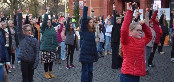 Viele Kinder und Erwachsene stehen auf einem Platz und heben den rechten Arm hoch.