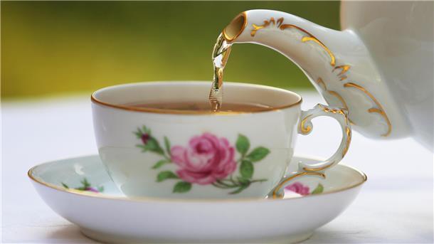 Tee wird aus einer Kanne in eine Tasse gegossen.